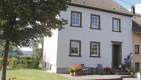 Een charmant, tweeledig huis met witte muren en bruine raamkozijnen. Voor het huis staan tuinmeubels en kleurrijke bloemen in potten.