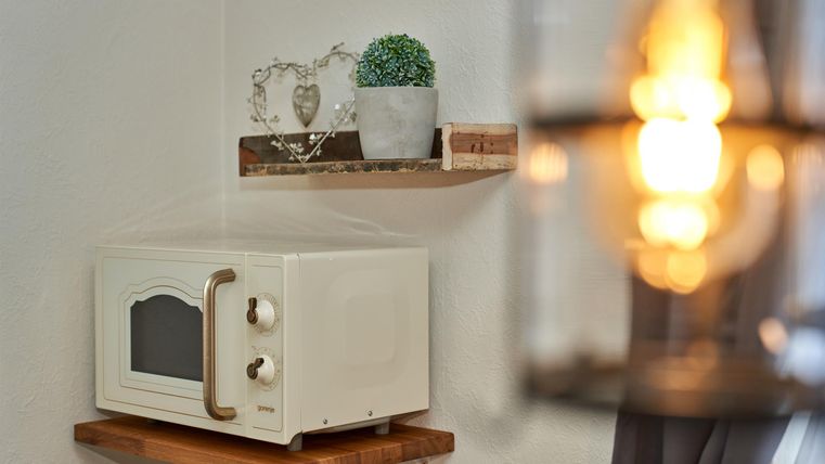Eine Mikrowelle steht auf einem Holzregal an der Wand. Darüber sind Pflanzen und dekorative Objekte auf einem weiteren Regal platziert.