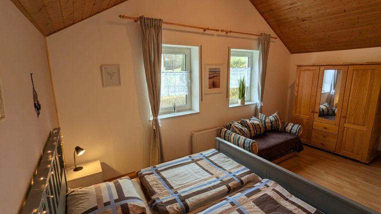 Ein helles Schlafzimmer mit zwei Betten und einem gemütlichen Stil. Es gibt große Fenster, einen Kleiderschrank und eine Sitzecke.