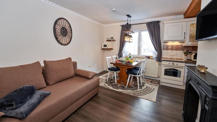 Ein gemütliches Wohnzimmer mit einem braunen Sofa und einem Esstisch. Die Küche ist gut ausgestattet und das Fenster lässt viel Licht herein.