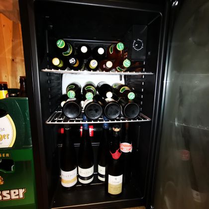 Ein Kühlschrank voller Flaschen, darunter Bier und verschiedene Weine. Die Flaschen sind ordentlich auf zwei Regalen angeordnet.