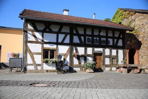 <p>Ein Fachwerkhaus mit dem Schriftzug "Backhaus" über der Eingangstür unter blauem Himmel.</p>