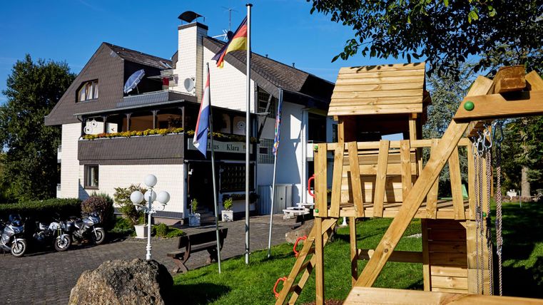 Ein modernes Gebäude mit einer Spielanlage im Vordergrund. Flags und Motorräder sind ebenfalls sichtbar, umgeben von Grünflächen.