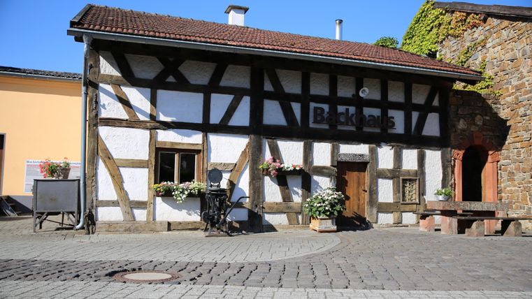 Ein traditionelles Fachwerkhaus mit einem einladenden Eingangsbereich. Blumen schmücken die Fenster und der Pflasterweg ist gut gepflegt.