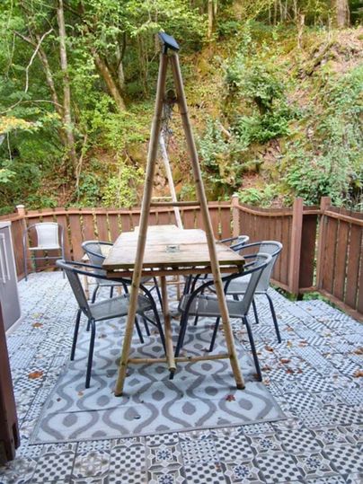 Ein gemütlicher Terrassenbereich mit einem Holztisch und sechs Stühlen. Umgeben von Bäumen und einer ruhigen, grünen Landschaft.