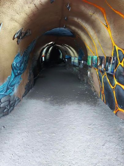 Ein langer, schmaler Tunnel mit bunten Wandmalereien. Der Boden ist weitgehend schotterig und es gibt Kunstwerke an den Wänden.