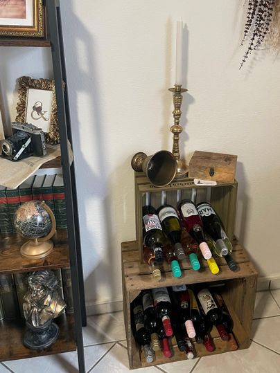 Ein stilvolles Weinregal aus Holz mit mehreren Flaschen Wein. Darüber steht eine elegante Kerze und ein Messinggegenstand.