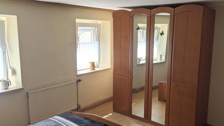 Ein Schlafzimmer mit einem großen, hellen Kleiderschrank und zwei Fenstern. Die Wände sind in neutralen Farben gehalten und der Boden ist aus Holz.