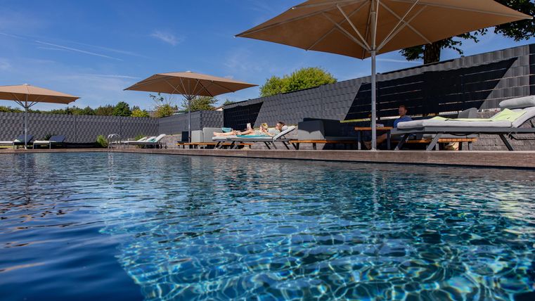 Ein schöner Pool mit Liegen und Sonnenschirmen. Der Himmel ist klar und blau, ideal zum Entspannen.