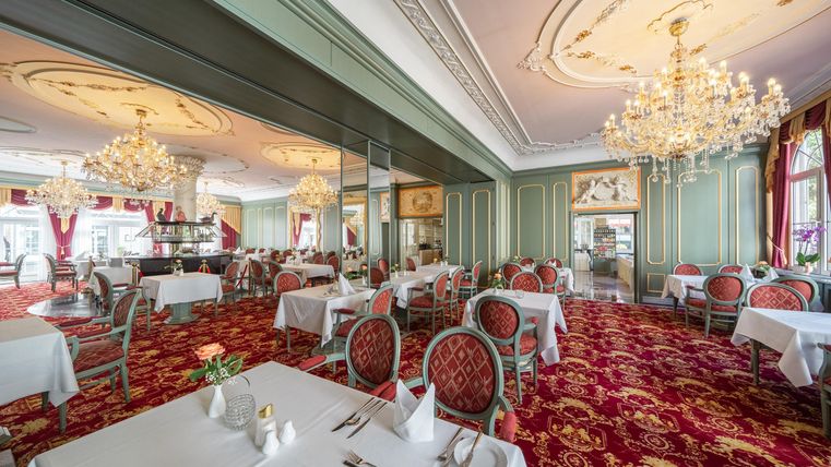 Ein elegantes Restaurant mit stilvollen Tischen und roten Teppichen. Funkelnde Kronleuchter beleuchten den Raum und schaffen eine gemütliche Atmosphäre.