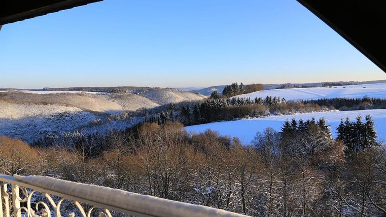 A winter view of snow-covered hills and forests. The clear blue sky complements the peaceful landscape.