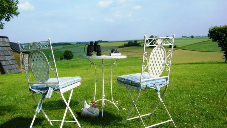 Ein schöner Tisch mit zwei Stühlen im Freien, umgeben von einer grünen Landschaft. Auf dem Tisch liegen ein Fernglas und einige Bücher.