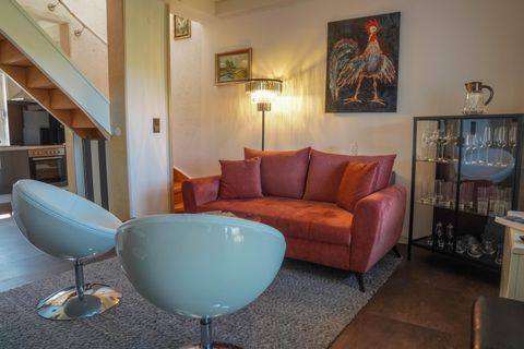 Ein modernes Wohnzimmer mit einem rosa Sofa und zwei blauen Stühlen. An der Wand hängt ein Gemälde eines Huhns, und es gibt einen Glastisch mit Gläsern.