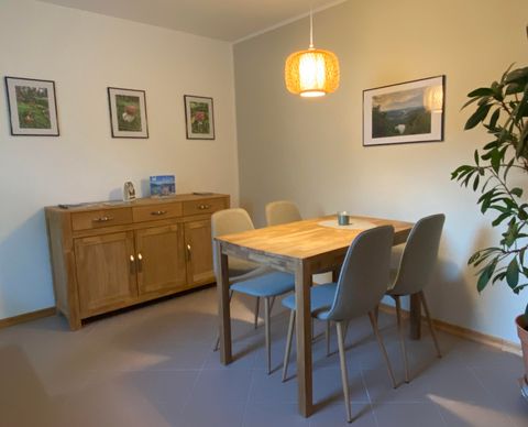 Ein einladender Essbereich mit einem Holztisch und modernen Stühlen. An der Wand hängen Bilder, und eine Pflanze sorgt für ein gemütliches Ambiente.