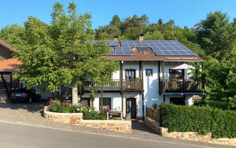 Ein modernes Haus mit Solarpanelen auf dem Dach. Es steht in einer ruhigen Umgebung mit grünen Bäumen und einem gepflegten Garten.