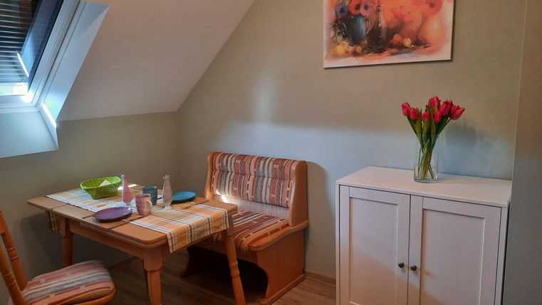 Ein gemütlicher Essbereich mit einem Holztisch und zwei Bänken. Auf dem Tisch stehen verschiedene Gegenstände und eine Vase mit roten Tulpen.