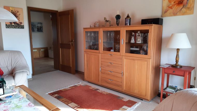 Ein gemütliches Wohnzimmer mit einem Holzschrank und einer roten Lampe. Durch die offene Tür ist ein weiterer Raum sichtbar.
