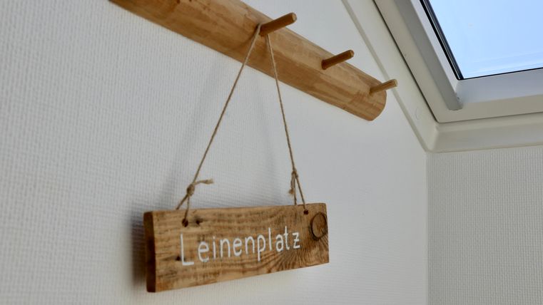 Ein Holzschild mit der Aufschrift „Leinenplatz“ hängt an einer Wand. Darüber befindet sich ein kleiner Holzkleiderhaken.