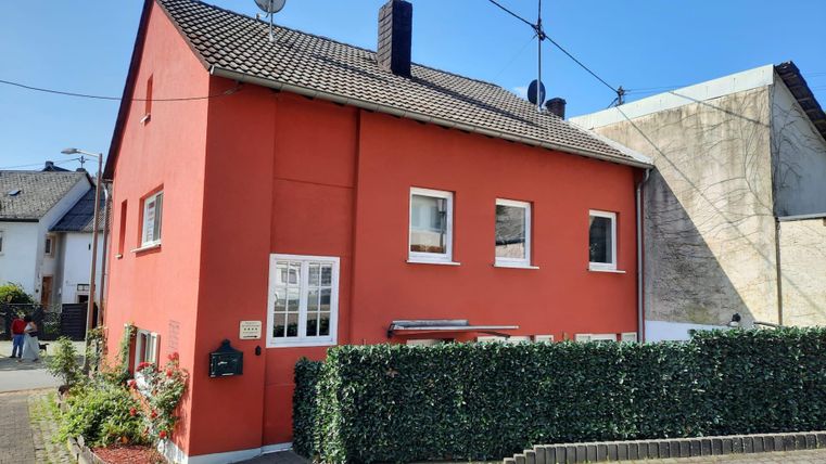 Ein rotes Haus mit einem gepflanzten Vorgarten. Es hat helle Fenster und eine klare blaue Himmel im Hintergrund.
