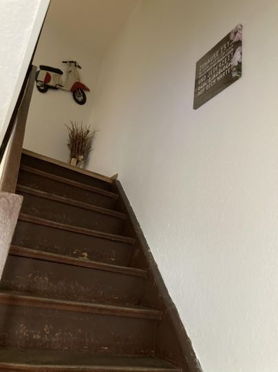 Eine Treppe mit Holzstufen führt nach oben. An der Wand hängt ein kleines Motorradmodell und eine Dekoration.