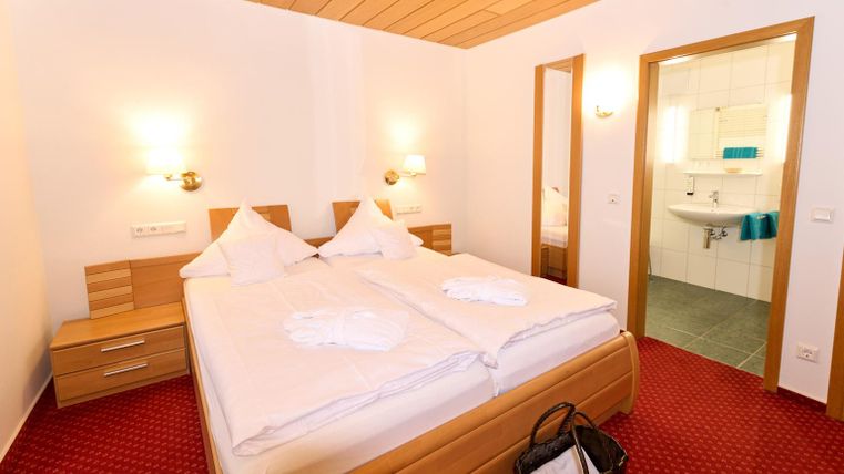 Ein gemütliches Schlafzimmer mit einem Doppelbett und warmem Holzdekor. Das Zimmer verfügt über zwei Nachttische und ein angrenzendes Badezimmer.