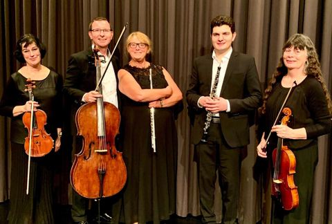 Eine Gruppe von fünf Musikern steht auf einer Bühne. Sie halten verschiedene Musikinstrumente und tragen elegante schwarze Kleidung.