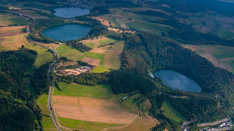 Eine beeindruckende Landschaft mit zwei blauen Seen und umgeben von grünen Wäldern und Feldern. Der Himmel ist klar, was die natürliche Schönheit der Region betont.