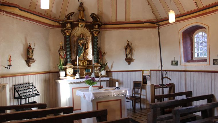 Eine kleine Kapelle mit einem Altar, umgeben von Holzsitzen. An den Wänden hängen religiöse Statuen und Bilder.