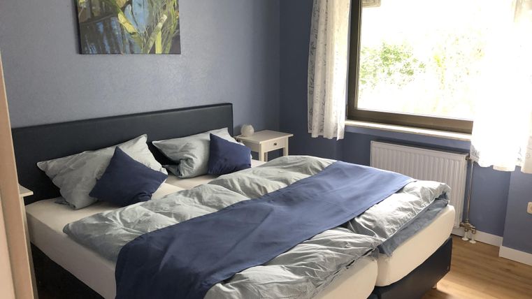 Ein gemütliches Schlafzimmer mit einem großen Doppelbett und blauen Bettwäsche. Das Zimmer hat eine Fensterfront mit viel Tageslicht und einem schönen Ausblick.