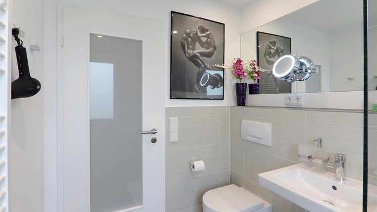Ein modernes Badezimmer mit eleganten Armaturen und einem großen Spiegel. Es gibt dekorative Pflanzen und Kunstwerke an der Wand.