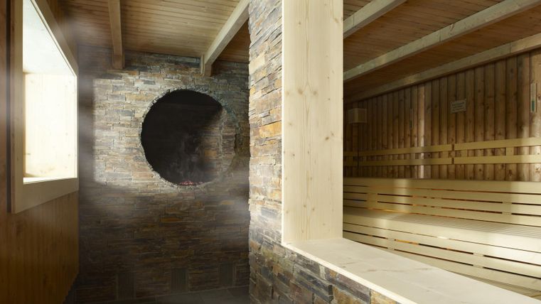 Ein heller Saunabereich mit Holz- und Steinmaterialien. Dampf ist vorhanden, und große Fenster sorgen für natürliches Licht.