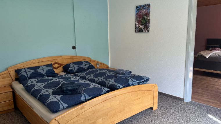 Ein modernes Schlafzimmer mit einem Doppelbett aus Holz und blauen Bettwaren. Die Wände sind in sanften Farben gestrichen und es gibt ein Fenster, das natürlichem Licht einlässt.