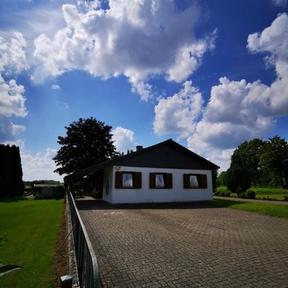 Ein schönes Einfamilienhaus mit einer großen Auffahrt. Der Himmel ist blau und von einigen schönen Wolken durchzogen.