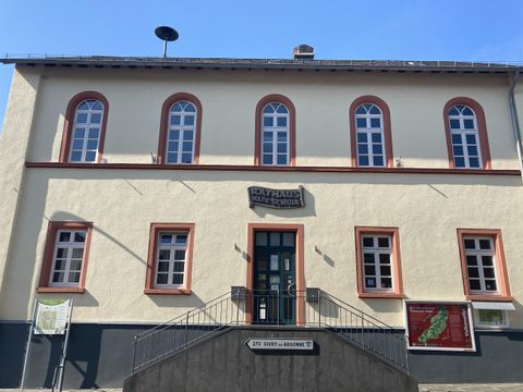 Ein Gebäude mit mehreren Fenstern und einem Eingang. Die Fassade ist hell mit roten Akzenten.