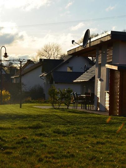Ein ruhiger Garten mit grünem Gras und mehreren Häusern im Hintergrund. Auf der Terrasse stehen Tische und Stühle.