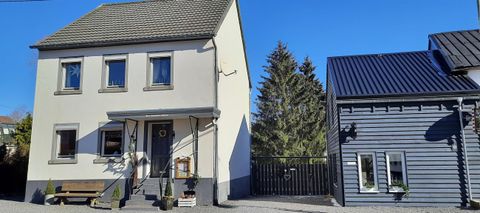 Ein modernes Haus mit einem klaren blauen Himmel im Hintergrund. Neben dem Haus steht ein zusätzliches Gebäude in dunkler Farbe.
