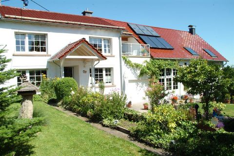 Ein schönes Haus mit rotem Dach und großen Fenstern. Der gepflegte Garten ist mit bunten Pflanzen und Bäumen umgeben.