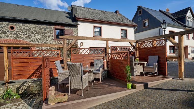 Eine einladende Terrasse mit mehreren Stühlen und einem Tisch. Umgeben von Holzlatten und einem klaren blauen Himmel.