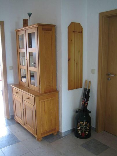 Ein freundlicher Flur mit einem Holzschrank und einem Wandregal. Auf dem Boden stehen ein paar Regenschirme.