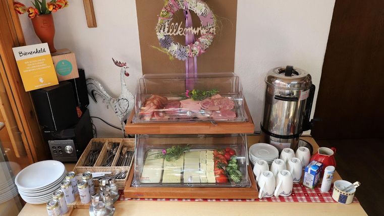 Ein Buffet mit verschiedenen Fleischsorten, frischem Gemüse und Käse. Darin befinden sich auch Kaffeekannen und Geschirr auf einem Tisch.