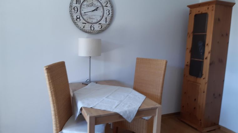 Ein gemütlicher Essbereich mit einem runden Tisch, zwei Stühlen und einer Stehlampe. An der Wand hängt eine große Uhr und ein Holzschrank steht neben dem Tisch.