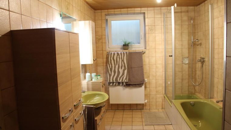 Ein modernes Badezimmer mit einer Dusche und einer Badewanne. Die Wände sind gefliest und es gibt Holz-Elemente sowie einen großen Spiegel.