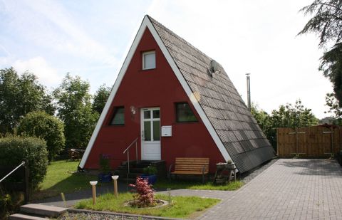A red, triangular holiday home with a sloping roof. Surrounded by a green garden and a terrace.