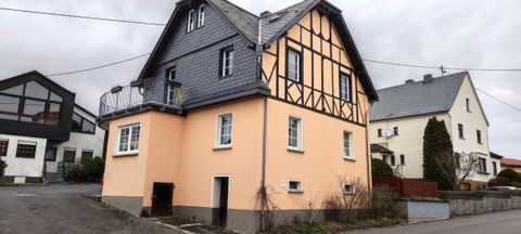 Ein charmantes Gebäude mit einer orangefarbenen Fassade und einem Giebeldach. Daneben sind weitere Häuser in einer ruhigen Straße zu sehen.
