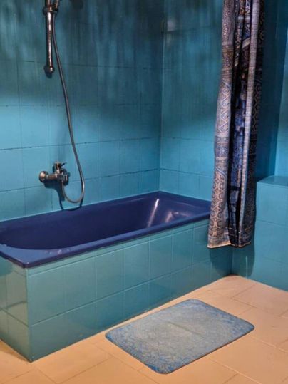 Ein modernes Badezimmer mit einer blauen Badewanne und einer Dusche. Die Wände sind in einem kräftigen Blauton gehalten, und ein Teppich liegt auf dem Boden.