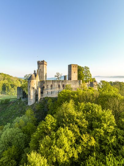 Aerial view of Kasselburg Castle in Pelm, surrounded by green trees and a clear sky.