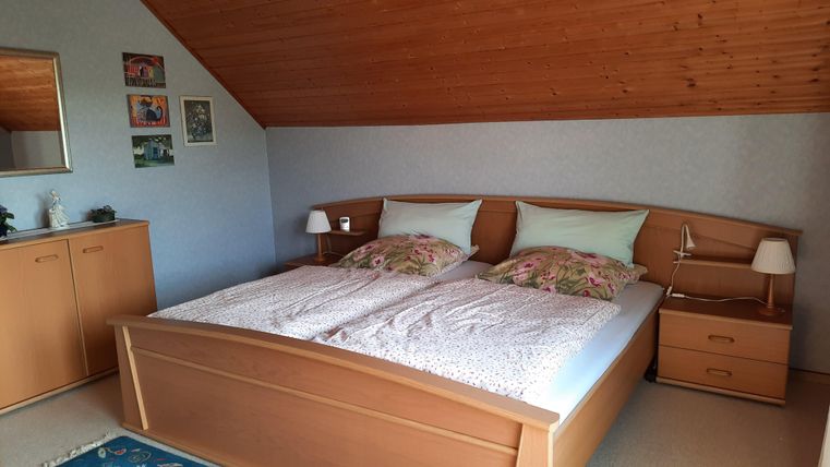Ein gemütliches Schlafzimmer mit einem großen Doppelbett. Die Wände sind hell, und es gibt einen Holzbereich mit Dekor und Möbeln.