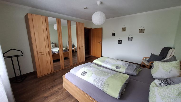 Ein gemütliches Schlafzimmer mit zwei Betten und einem Kleiderschrank aus Holz. Die Wände sind hell gestrichen, und es gibt eine angenehme, ruhige Atmosphäre.