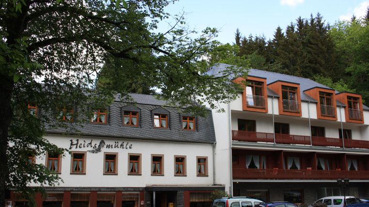 Ein charmantes Hotelgebäude mit zwei unterschiedlichen Architekturstilen. Das Gebäude ist von Bäumen umgeben, was eine ruhige Atmosphäre schafft.