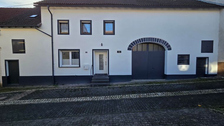 Een modern huis met een witte gevel en meerdere ramen. De voordeur is goed zichtbaar en er is ook een grote poort aanwezig.